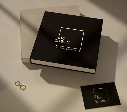 Ido Sitbon Photographers logo debossed in gold foil on a linen wedding album and on a gilded-edge card